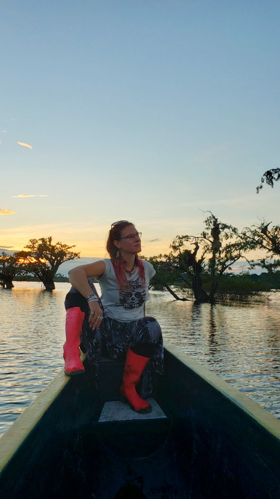 A girl sitting on a front of a small boat in a lake with tree tops coming out of the water. It's called the "Floating Forest" 